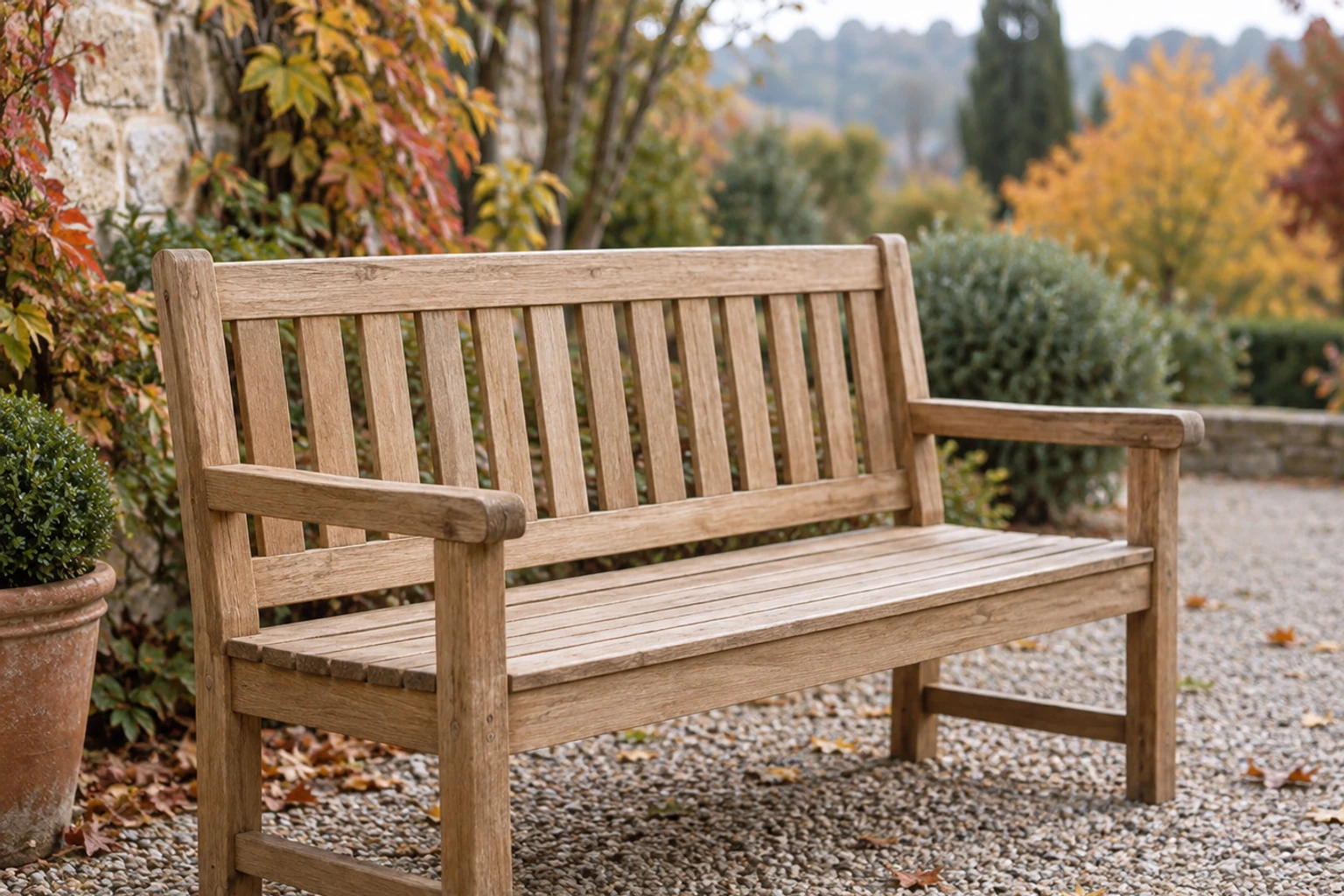 Holz-Gartenbank mit Lehne und Armlehnen auf Kiesplatz vor herbstlicher Bepflanzung